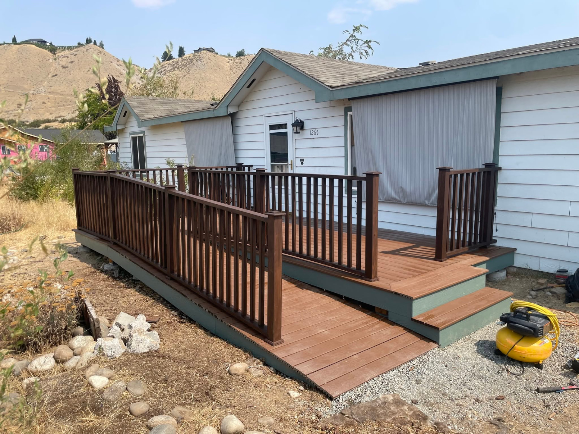 Brown deck with accessible ramp, steps and dark stained wood railing at a white house